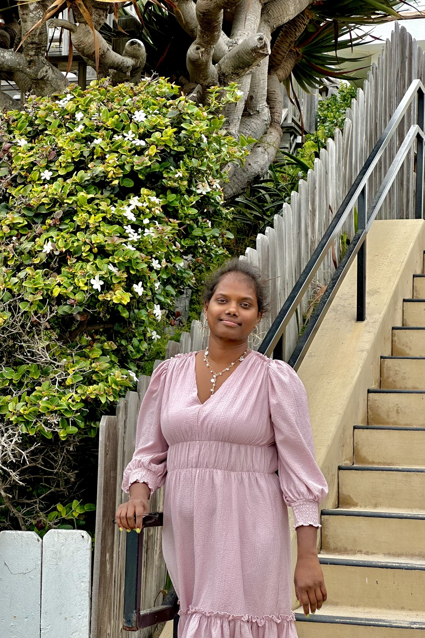 Prema Walker standing on garden steps beside a flowering shrub